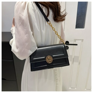 Detail of a black leather crossbody bag featuring a round vintage gold metal buckle and chain