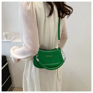 Green leather saddle bag detail with metal chain strap worn on a white pleated dress