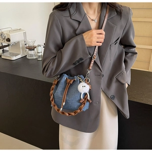 Detail of blue denim bucket bag with brown leather trim and cute white plush charm