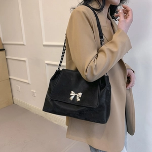Black flap shoulder bag with silver butterfly accent and chain strap worn by a model