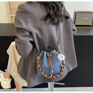 Denim bucket bag with braided leather handle and white pompom shown on a model