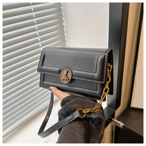 Detail of black crossbody bag featuring a bronze bear relief buckle and metal chain strap
