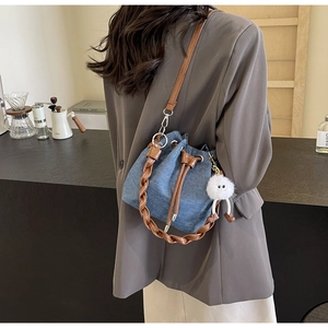 Detail of blue denim bucket bag with brown leather braided handle and plush eye charm