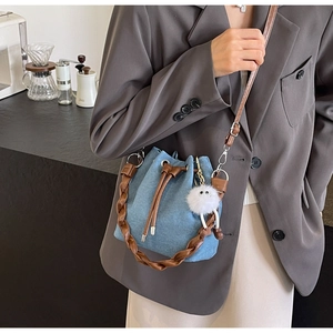 Blue denim bucket bag with woven leather handle and cute plush charm in cafe setting