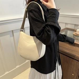 Minimalist beige pebble leather half-moon hobo bag with wide shoulder strap on model