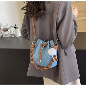 Blue denim bucket bag with brown woven handle and plush charm on a café background