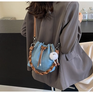 Detail of blue denim bucket bag with brown leather trim and cute white plush charm