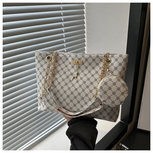 Detail of off-white tote bag with black clover pattern and golden chain strap