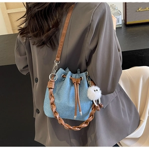 Detail of blue denim bucket bag with brown leather braided handle and white fur charm