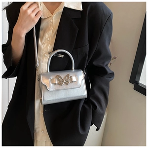Silver PU leather crossbody bag featuring a metallic butterfly clasp worn by a model