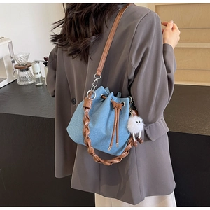Detail of blue denim bucket bag with woven handle and plush charm on a model