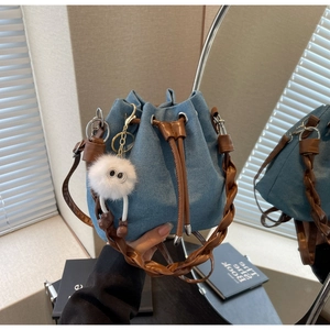 Detail view of denim bucket bag with woven handle, leather drawstring and plush monster charm