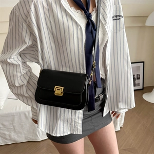 Minimalist black leather crossbody bag with gold buckle on a stylish model