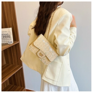 Detail of woven straw saddle bag with floral embroidery and golden metal chain strap