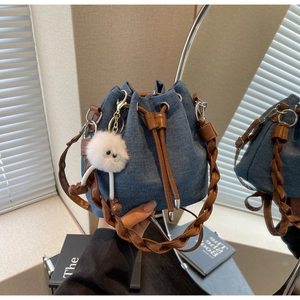 Detail of blue denim bucket bag featuring brown leather woven handle and plush charm