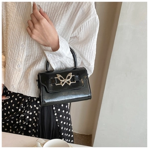 Detail of black patent leather crossbody bag with a gold butterfly metal clasp closure