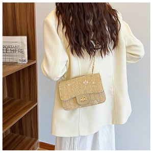 Detail of light beige straw crossbody bag featuring floral embroidery and gold chain strap
