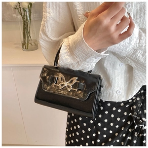 Close-up of black patent leather mini handbag with a silver butterfly metal buckle