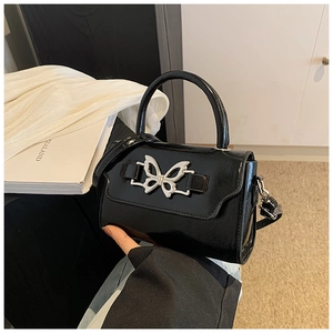 Detail of glossy black leather crossbody bag featuring a silver butterfly buckle closure