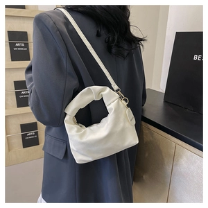 Detail of a creamy white cloud-shaped shoulder bag with pleated handle on a model