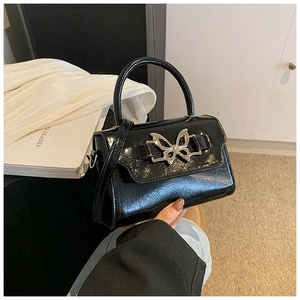 Detail of glossy black leather crossbody bag featuring a silver butterfly metal buckle