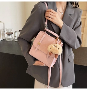 Pink matte leather crossbody bag with round metal buckle and plush charm detail