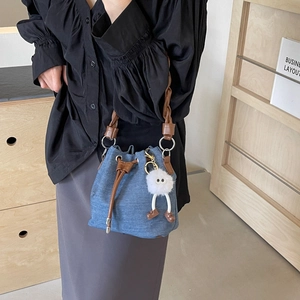 Blue denim bucket bag with brown leather handles and a plush doll charm on a model