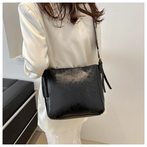 Polished black leather tote bag worn over the shoulder by a model in a white blazer