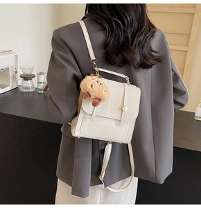 Close-up of a white leather backpack with metal clasp and brown plush charm on a model