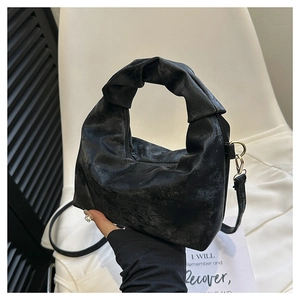 Detail of matte black handbag with vintage texture, knotted handle, and gold buckle