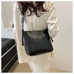 Close-up of black glossy bucket bag with textured leather and checkered shoulder strap