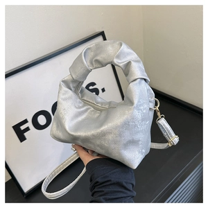 Close-up of silver metallic handbag with twisted handle and detachable crossbody strap