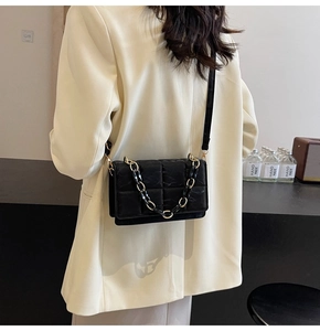 Sac bandoulière matelassé noir avec chaîne dorée porté sur un tailleur chic