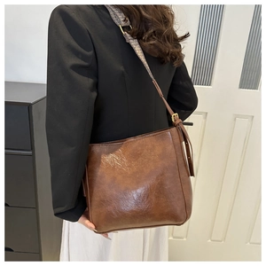 Detail of dark brown glossy bucket bag with patterned wide strap on a model shoulder