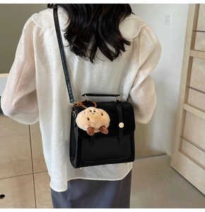 Detail of black PU leather shoulder bag with gold clasp and fun plush potato charm