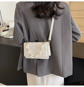 Détail du sac bandoulière blanc matelassé avec chaîne en résine porté par un mannequin