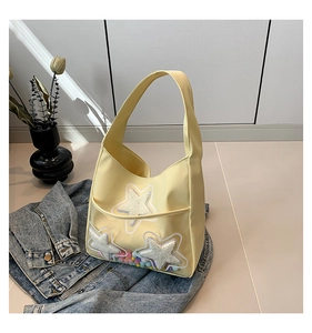Détail du sac cabas jaune avec étoiles en peluche et pompons colorés dans la poche basse