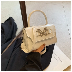Close-up of a white glossy leather square bag featuring a delicate metal butterfly buckle