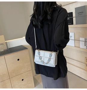 Détail d'un sac bandoulière argenté matelassé avec une chaîne décorative bleue et dorée