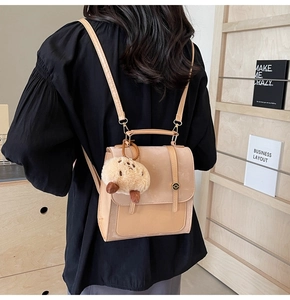 Detail view of a beige faux leather backpack with plush bear charm on back of person