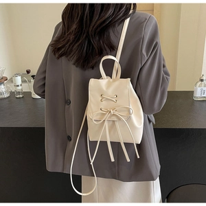 Detail of a creamy white mini backpack with a decorative bow and metallic eyelets