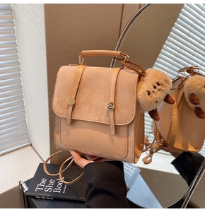 Detail view of beige leather backpack showing matte texture and plush animal charm