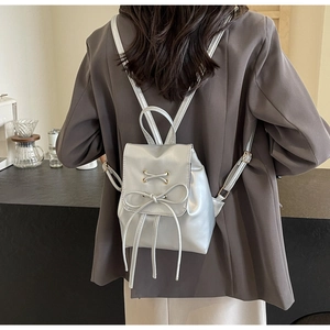 Detail of silver mini backpack with bow decoration worn by model in minimalist setting