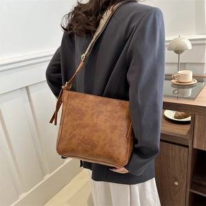 Vintage brown leather tote bag with adjustable strap worn by a model in a cozy room