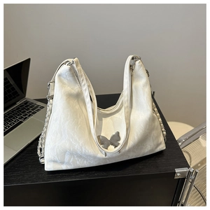 Détail d'un sac à main blanc plissé avec boucle papillon argentée sur un bureau en bois