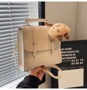 Detail of off-white vintage backpack with golden buttons and a plush dog charm