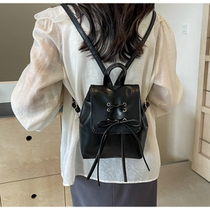 Detail of black mini backpack featuring decorative bow and metallic eyelets on flap cover