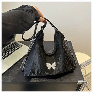Détail d'un sac cabas plissé noir avec breloque papillon argentée et bandoulière chaîne
