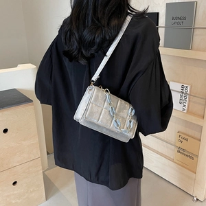 Sac bandoulière argenté matelassé avec chaîne acrylique bleue porté par un mannequin