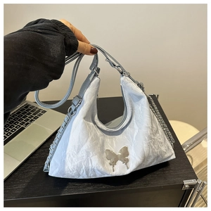 Détail d'un sac à bandoulière plissé bleu clair avec papillon argenté et chaîne